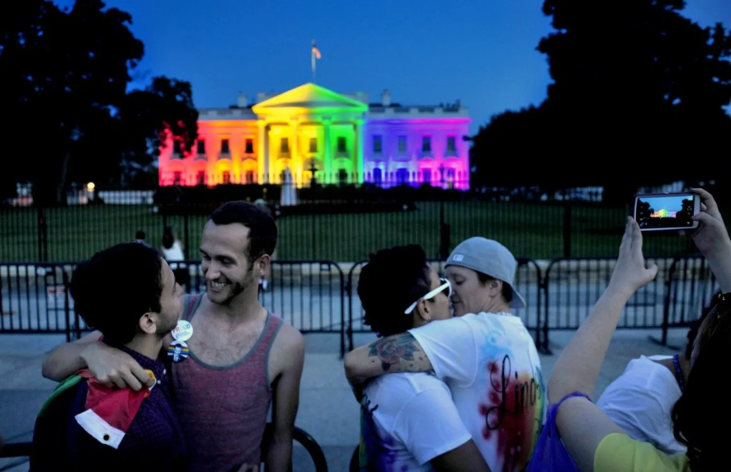 People celebrating in front of the white house illuminated in rainbow colors.