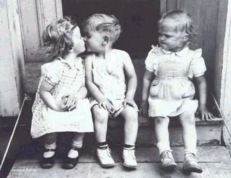 Two toddlers kissing while another looks on with a surprised expression.