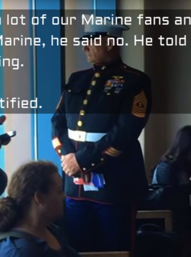 U.s. marine in dress uniform standing in a room with seated guests.