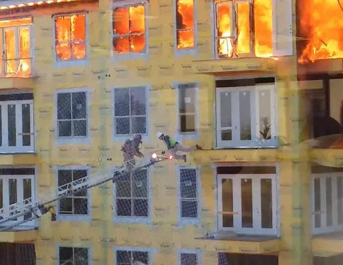 Firefighters on a ladder rescuing a person from a burning building.