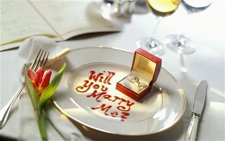 Romantic marriage proposal at a dinner setting with an engagement ring and "will you marry me?" written in sauce.