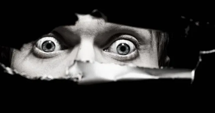 Person peeking through a tear in black material with wide eyes.