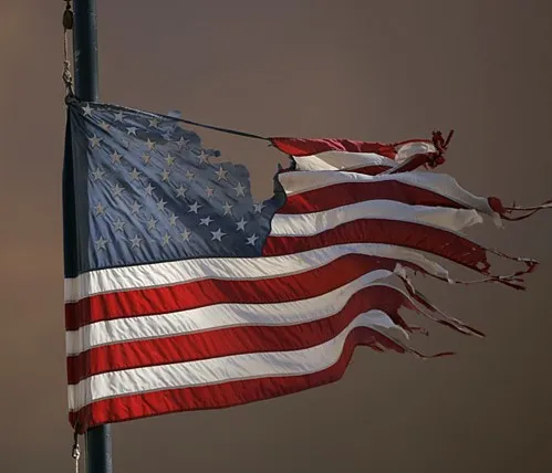 A tattered american flag waving on a pole.