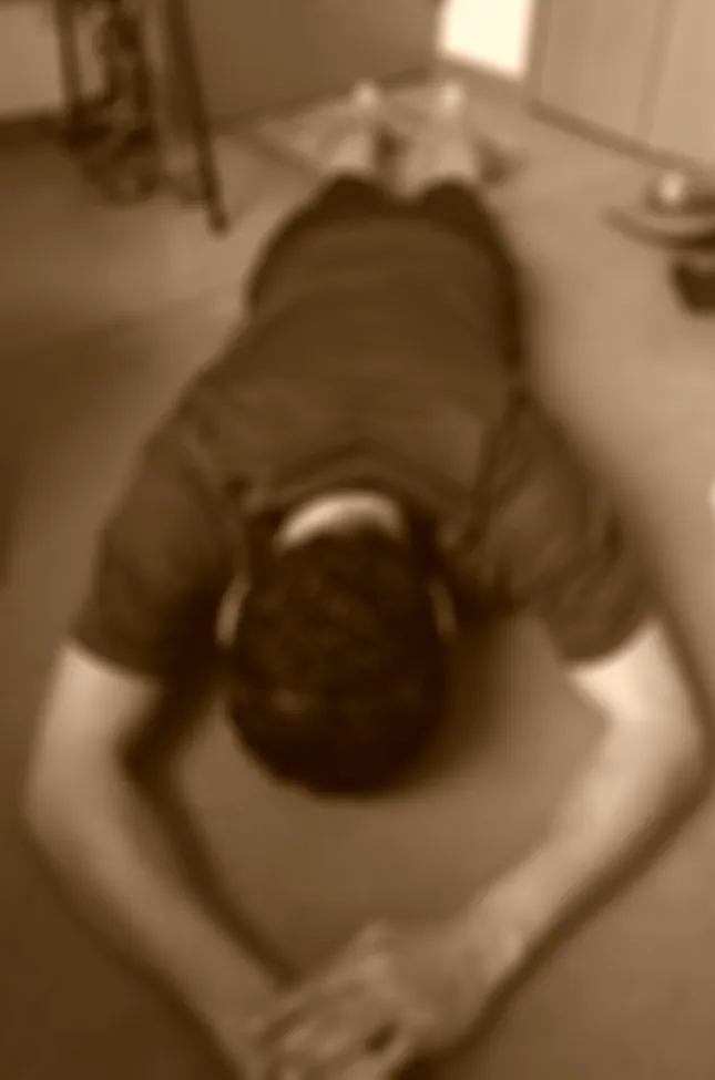 Due to the low resolution and blurriness of the image, it's difficult to discern precise details, but it appears to be a person lying face down on a mat on the floor.