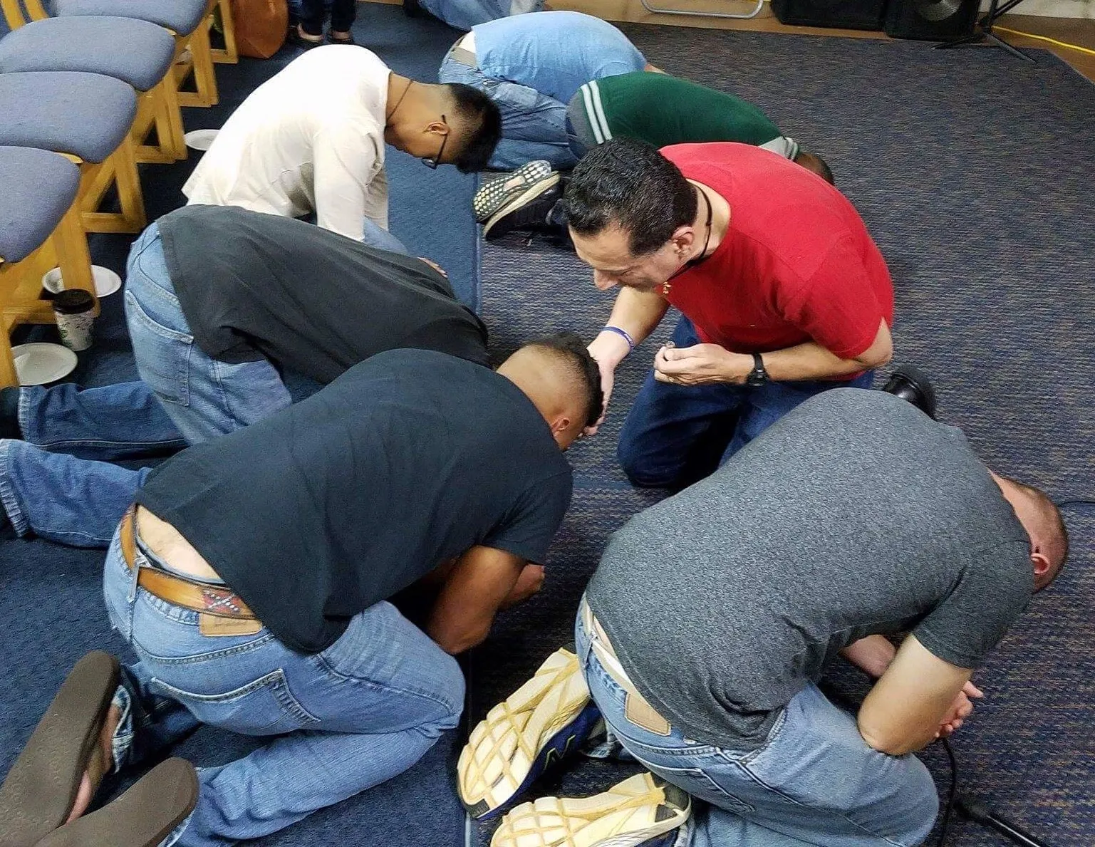 Group of men bowing their heads in prayer.