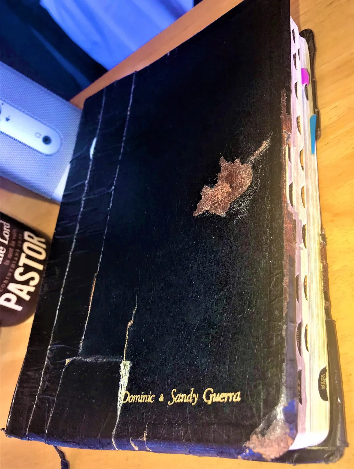 A well-used book with a black cover, visible wear and tear, and tabbed pages resting on a wooden surface.