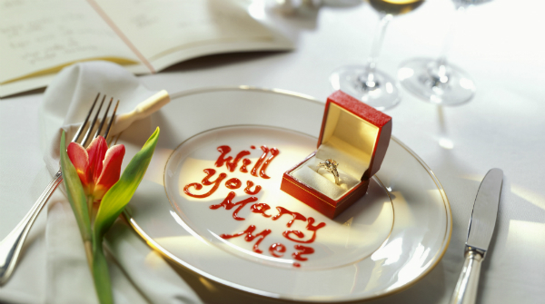 Marriage proposal at a restaurant with ring and "will you marry me?" written in sauce.