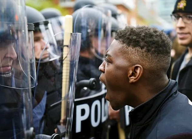 A young man confronts a line of police officers equipped with riot shields.