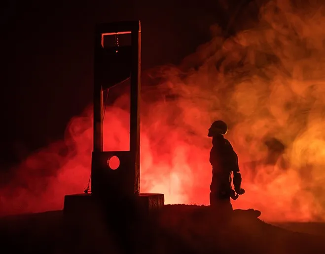 Firefighter standing near a burning structure at night.