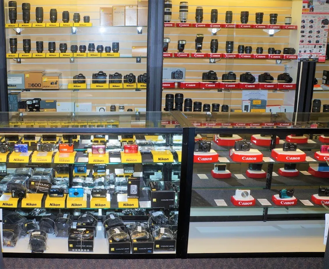 Display of various cameras and photography equipment on shelves in a retail store.