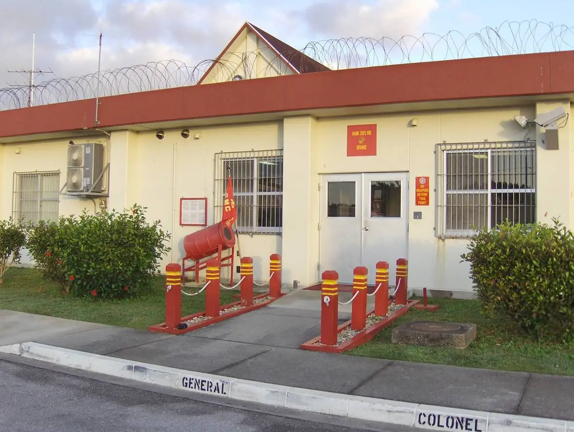 A single-story building with red and yellow barriers, barbed wire on the roof, and designated parking signs for "general" and "colonel.