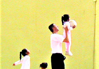 An adult lifting a child toward a basketball hoop as two other children watch.