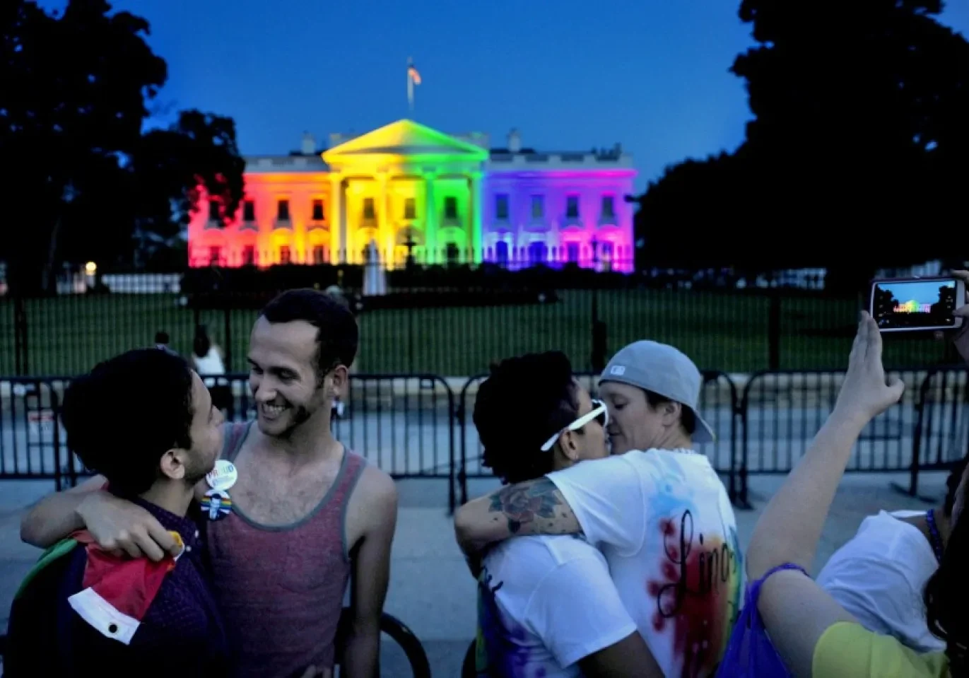 People celebrating in front of the white house illuminated in rainbow colors.