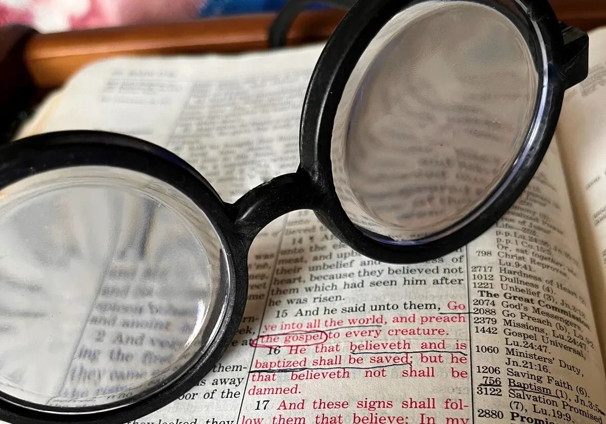 Round glasses resting on an open bible with text in focus through the lenses.