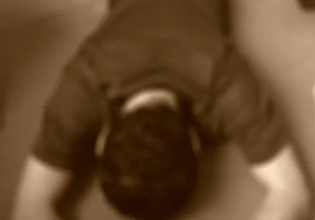 Due to the low resolution and blurriness of the image, it's difficult to discern precise details, but it appears to be a person lying face down on a mat on the floor.