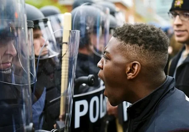 A young man confronts a line of police officers equipped with riot shields.