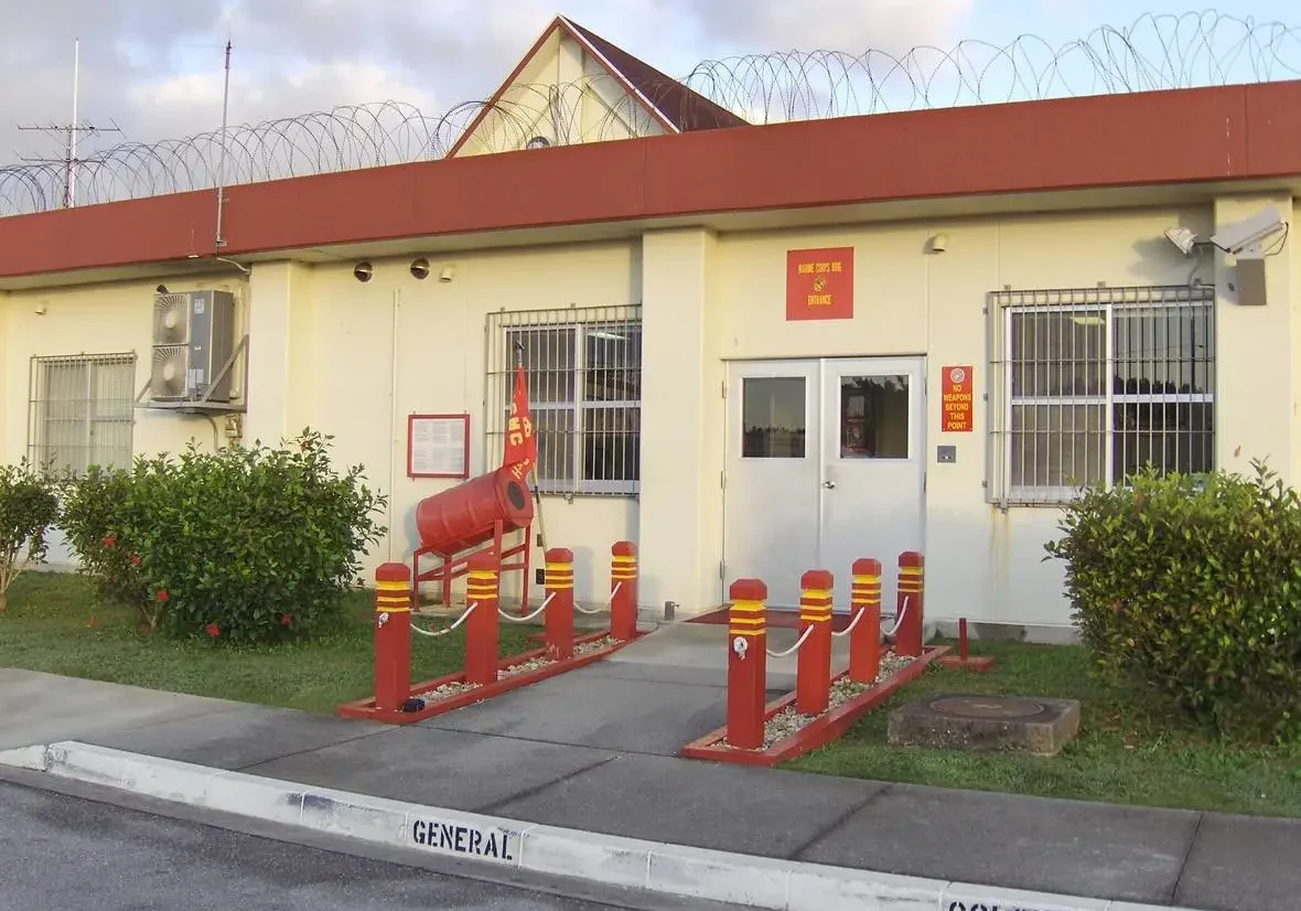 A single-story building with red and yellow barriers, barbed wire on the roof, and designated parking signs for "general" and "colonel.