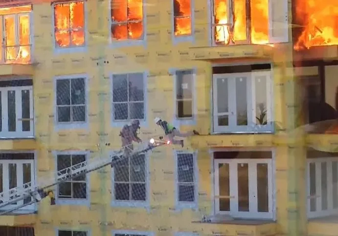 Firefighters on a ladder rescuing a person from a burning building.