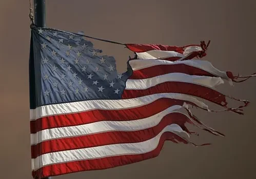 A tattered american flag waving on a pole.