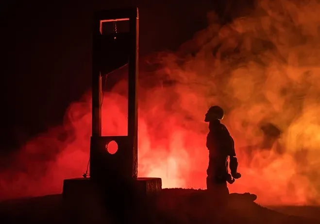 Firefighter standing near a burning structure at night.