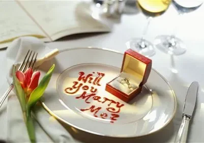 Romantic marriage proposal at a dinner setting with an engagement ring and "will you marry me?" written in sauce.