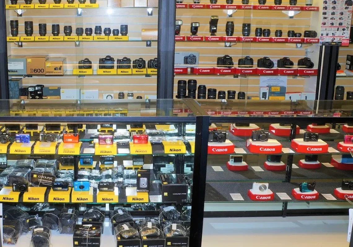 Display of various cameras and photography equipment on shelves in a retail store.